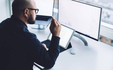 İş sırasında tablet kullanırken masanın üzerinde oturan ve laptopta bilgi sörfü yapan tanınmayan erkek çalışanlardan.