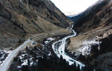 Yukarıdan dar asfalt bir yoldan karlı dağ sırasındaki Alpler vadisinde bulutlu bir günde kozalaklı ağaçlarla ilerliyor.