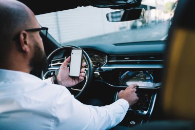 Kimliği belirsiz erkek sürücünün arabada otururken radyo kanalı değiştirmesi ve şehirde eve dönerken akıllı telefon tutması.