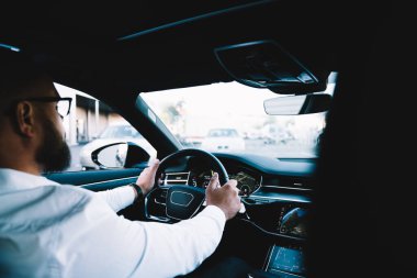 Kenarda, direksiyon tutarken ve şehir caddesinde araba kullanırken tanınmayan bir erkeğin modern araba kullanışının yan görüntüsü.