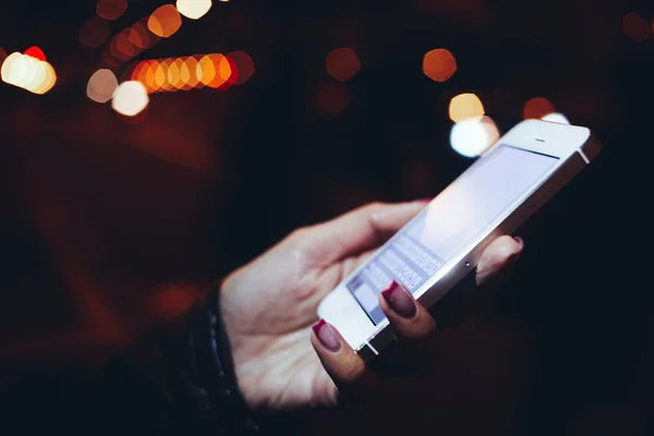 夜間ライトアップされた街の通りに立っている間 携帯電話とテキストメッセージを使用して黒い革のジャケットの作物顔のない女性 — ストック写真