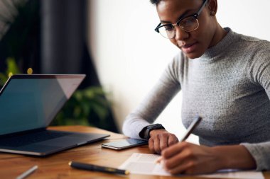 Gündelik giysiler ve gözlükler içinde genç etnik kadın işçiler masada oturup dizüstü bilgisayarla araştırma yaparken düşüncelerini yazıyorlar.