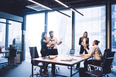 Sınıftaki çeşitli yoğun iş arkadaşları toplantı odasında birlikte çalışırken ve birbirleriyle iletişim kurarken iş stratejileri hakkında konuşuyorlar.