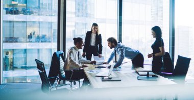 Modern ofiste cam duvarla çalışan çok ırklı genç meslektaşlar ön plandaki bulanıklık konusunda yoğun bir şekilde konuşuyorlar.