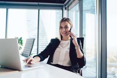 Sınıftaki genç zarif bayan girişimci toplantı odasındaki masada otururken netbook kullanıyor ve cep telefonuyla sohbet ediyor.