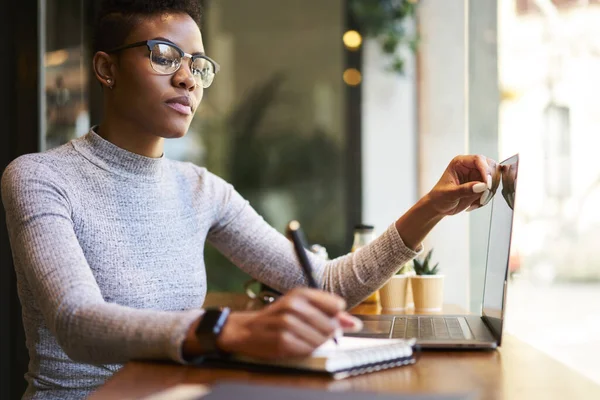 Konzentrierte Afroamerikanerin Lässiger Kleidung Sitzt Holztisch Mit Laptop Und Schreibt — Stockfoto