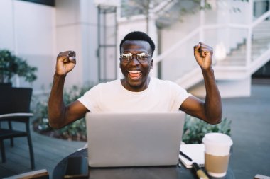 Gözlüklü mutlu koyu tenli erkek blogger portresi başarılı bir projeyi kutluyor Kafe terasında uzaktan çalışıyor, gülümseyen Afrikalı Amerikalı genç bir adam video oyununda zaferin tadını çıkarıyor