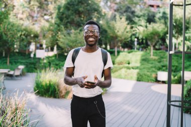 Koyu tenli erkek milenyum akıllı telefonunun yarım boy portresi 4G aracılığıyla mesaj gönderiyor, gülümseyen Afrikalı Amerikalı adam sosyal ağlarda sohbet ederek şehir ortamlarında günün tadını çıkarıyor.