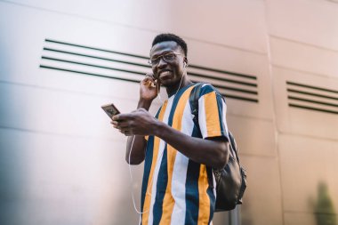 Düşük açılı, gülümseyen, Afro-Amerikan bir erkeğin sosyal medyada arkadaşıyla konuşması ve duvarın önündeki kameraya bakması.