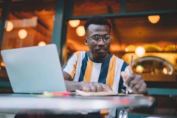 Seriöser Schwarzer Student Gestreiftem Shirt Und Brille Macht Sich Notizen — Stockfoto