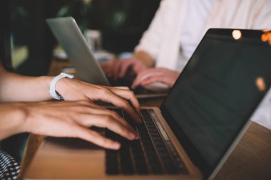 Fikirlerle paylaşırken dizüstü bilgisayarları kullanarak ahşap tezgahta oturan ve internette gezinen ortakların ekin kenarı görünümü 