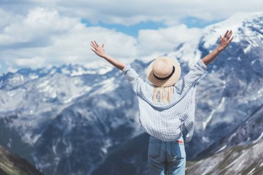 Şapkalı ve günlük kıyafetli sıska bir kadının arkadan görünüşü. Kollarını kaldırıp güneşli bir günün tadını çıkarırken aynı zamanda Lago di Braies 'in arka planında dikiliyordu.