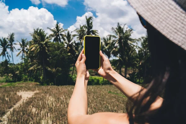 バリ島の夏休みに一人で休んでいる間 携帯電話で熱帯植物の写真を撮る帽子の女性観光客をトリミングします — ストック写真