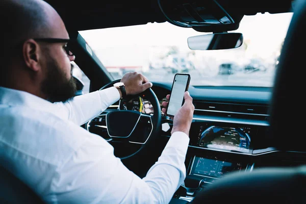 Back view of male driver reading received email message while steering automotive vehicle, employer in white shirt checking mobile time via cell application while lateness to business meeting