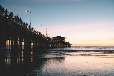 Huzurlu bir akşamda dinlenirken üzerinde yürüyen insanların olduğu ahşap iskele ve muhteşem renkli günbatımı gökyüzüne hayranlıkla bakıyorlar.