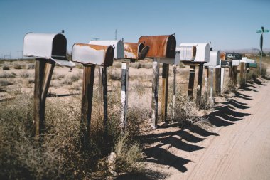 Kuru vadinin yol kenarına yerleştirilmiş eski yalnız posta kutuları boş sokaktaki kuru çimlerde mavi bulutsuz gökyüzüne karşı