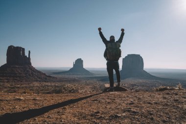 Gündelik giysiler ve sırt çantalı, kollarını kaldırıp anıt vadisindeki başarısını kutlayan yüzsüz erkek gezginin arka planı.
