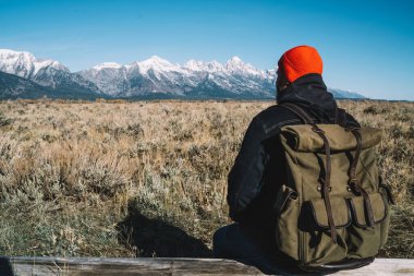Sıcak kıyafetler içinde, sırt çantalı, sırt çantalı, kırsal bölgelerdeki dağlara bakan tanınmamış bir erkek gezginin arka plan görüntüsü.
