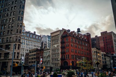 New York şehrinde bulutlu gökyüzüne karşı eski taş binalar ve kalabalık caddede yüksek kule bulunan yerleşim yeri.