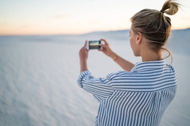 Alçıtaşı kum tarlasına karşı duran ve New Mexico 'daki White Sands Ulusal Parkı' nda telefonla fotoğraf çeken kadın kaşifin yumuşak odağı.