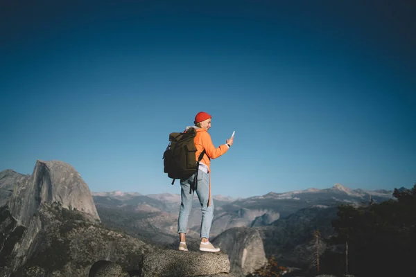 在约塞米蒂国家公园 身穿休闲装 头戴背包 站在岩石上浏览智能手机的女性游客的背影 — 图库照片