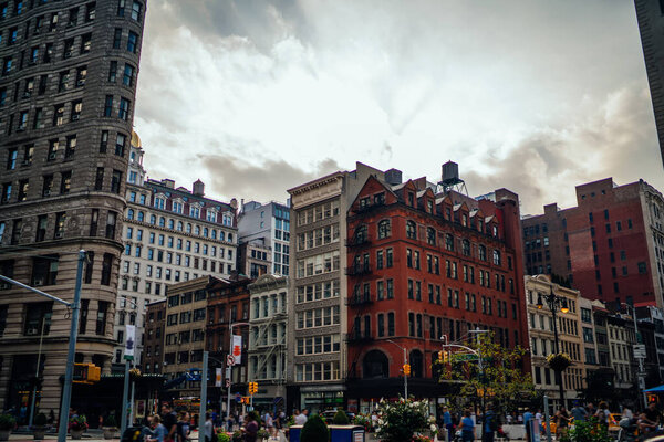 Residential area with old stone buildings and tall tower on crowded street against cloudy sky in city of New York