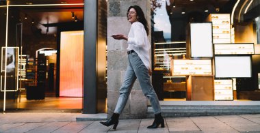 Tüm vücudu sıradan kıyafetler ve gözlüklerle mutlu bir kadın. Asfalt sokakta butiklerle yürüyor ve şarkı söylerken kulaklıkla müzik dinliyor.