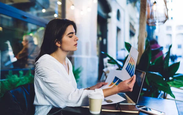 Side view of intelligent female professional checking profitable marketing analytic during remote working at terrace, Caucasian freelancer analyzing informative graph charts and revenue strategy