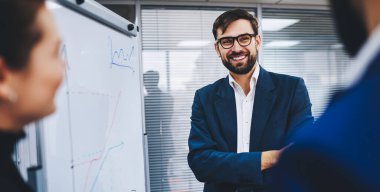İş arkadaşlarıyla sunum sırasında gülümseyen neşeli şirket lideri, resmi kıyafet giymiş mutlu iş adamı ve kırpılmış ortaklarla ekonomik grafikleri tartışan gözlüklü adam.