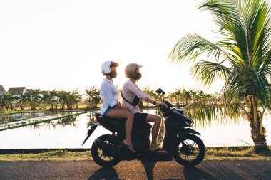 Miğferli ve maskeli, sakin göletin yanında bisiklet süren ve dinlenirken yüzünü çeviren tanınmayan bir çiftin yan görüntüsü