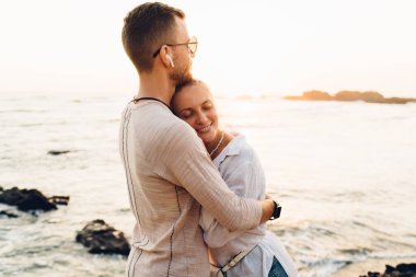 Tatmin olmuş kadın turist, tropik bir ülkede yaz akşamında erkeklerle kucaklaşırken boş gözlerle boş sahilde dikiliyor.