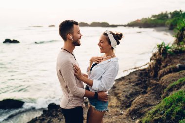 Hafta sonu boyunca kumsalda birlikte şarkı söylerken, mutlu bir kadının yanında duran, kablosuz kulaklıklı neşeli adamın yan görüntüsü.