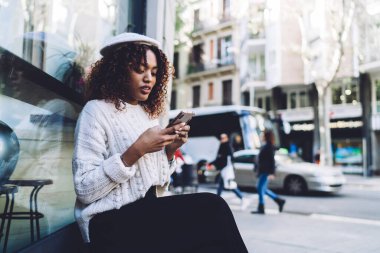 Oldukça koyu tenli kadın nüfuzlu kişi şehirdeki bankta oturan, Afro-Amerikan yenilikçi kız mesajları okuyarak ve akıllı telefondan 4G ile mesajlar göndererek sosyal ağlardaki içeriği paylaşıyor.