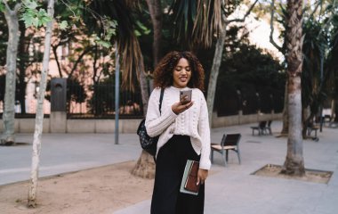 Sokakta boş duran, meşgul görünen, cep telefonlarını karıştıran ve internet iletişiminin keyfini çıkaran gündelik kıyafetli genç siyahi kadın.