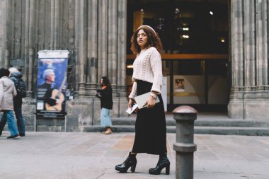 Modayı takip eden çekici, esmer tenli bir kadın şehirde tanınmış yerlerin yakınında yürürken giyindi. Güzel Afrikalı Amerikalı 20 'li yaşlarda bir kadın şehir ortamında geziniyor. Boş zamanlarını dışarıda geçiriyor.