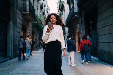 Moda giyinmiş, koyu tenli bir kadın ellerinde akıllı telefonlar, oyuncudan şarkılar seçerek, cep telefonu uygulaması üzerinden müzik dinleyen Afrikalı Amerikalı bir kadın.