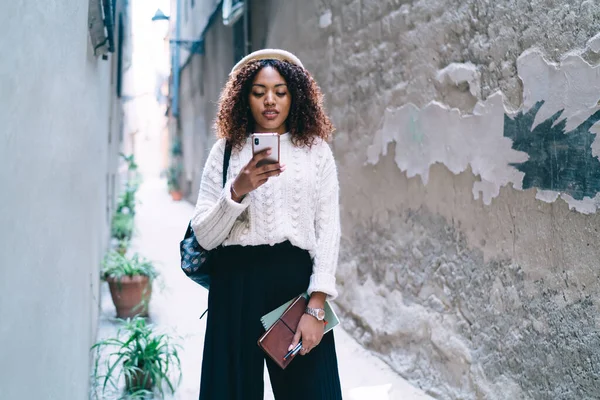 非洲裔美国女人 穿着时髦的衣服 一边用手机发短信 一边提着记事本 一边走在旧城 — 图库照片