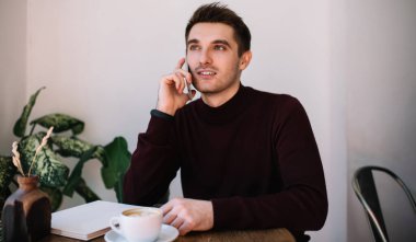 Kafeteryada sabah kahvesi sırasında danışmanlık yapmak için cep telefonu kullanan beyaz erkek öğrenci. Akıllı telefon uygulaması ile konuşmak için 30 yaşında yakışıklı bir gazeteci.