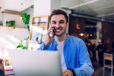 Komik erkek bilişim uzmanının portresi kameraya gülümserken aynı zamanda arkadaş canlısı cep telefonuyla konuşan neşeli bir adam web projesini tartışmak için mobil iletişim kuruyor.