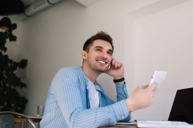 Işık duvarının önünde oturmuş mutlu mesut uzaklara bakarken, elinde küçük tabletlerle gülümseyen genç erkek.