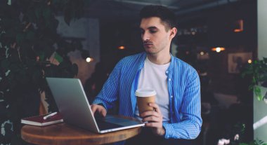 Kafkas erkek IT profesyonel kontrol programı metni modern dizüstü bilgisayarda kahve dükkanında mesafeli iş yapıyor, yakışıklı bir adam uygulama platformu üzerinden internetten web webinar izliyor.