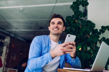 İnternette sörf yapan neşeli iş adamlarından cep telefonuyla açık bir dizüstü bilgisayarın önünde otururken ve başka yere bakarken.