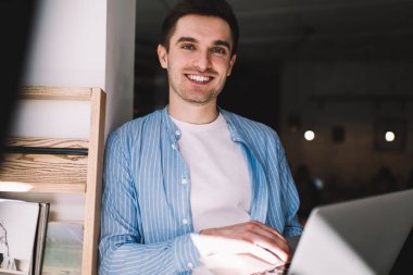 Ortak çalışma alanında poz veren modern netbook 'lu neşeli hipster adam portresi, 4G internet ve dizüstü bilgisayar uygulamaları ile uzaktan çalışan yarım boy mutlu erkek metin yazarı.