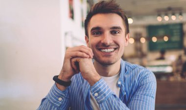 Boş zamanlarında kafeterya masasında el ele tutuşan neşeli Kafkasya 'nın yarım boy portresi, modaya uygun mavi gömlekli zengin bir erkek kameraya gülümseyip kahve dükkanında poz veriyor.