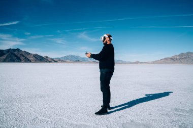 ABD seyahati sırasında sanal gerçeklik alanını izlerken, elinde kontrolör tutan ve tuz gölü üzerinde VR gözlük kullanan tanınmayan bir adamın yan görüntüsü