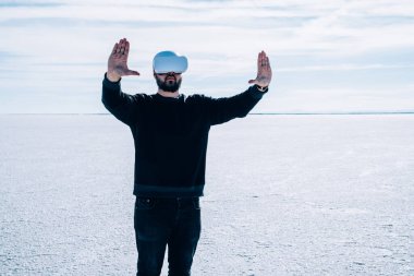 Sakallı erkek turist, kollarını kaldırmış Utah 'ta tuz düzlüğünde dururken gözlüklerle sanal gerçeklikle etkileşime geçiyor.