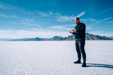 Amerikan Bonneville Tuz Düzlükleri 'ni keşfederken gündelik giyimli, taşınabilir kablosuz tabletli sakallı bir erkeğin yan görüntüsü.