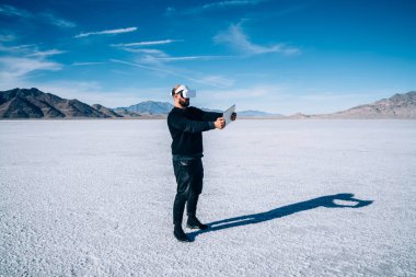 ABD 'nin Bonneville Tuz Düzlükleri' nde dinlenirken test oyunu için tablet kullanan, VR gözlüklü tanımlanamayan bir erkek.