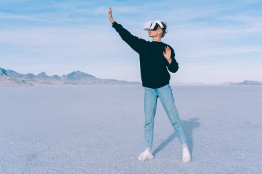 Sıradan giyinen anonim kadın, Bonneville ABD 'deki Salt Flat' te bulutlu gökyüzüne karşı sanal gerçeklik kulaklığı denerken poz veriyor.