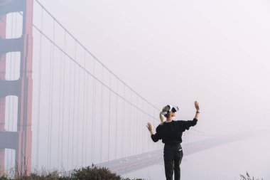 San Francisco 'da sanal gerçekliği keşfederken Golden Gate Köprüsü yakınlarında VR gözlüğü takan kimliği belirsiz bir kadının arka plan görüntüsü